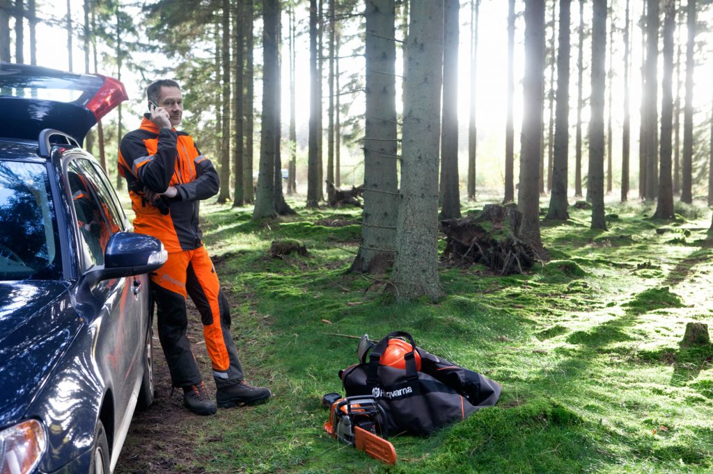 Forestry worker leaning against his car, talking in a mobile phone