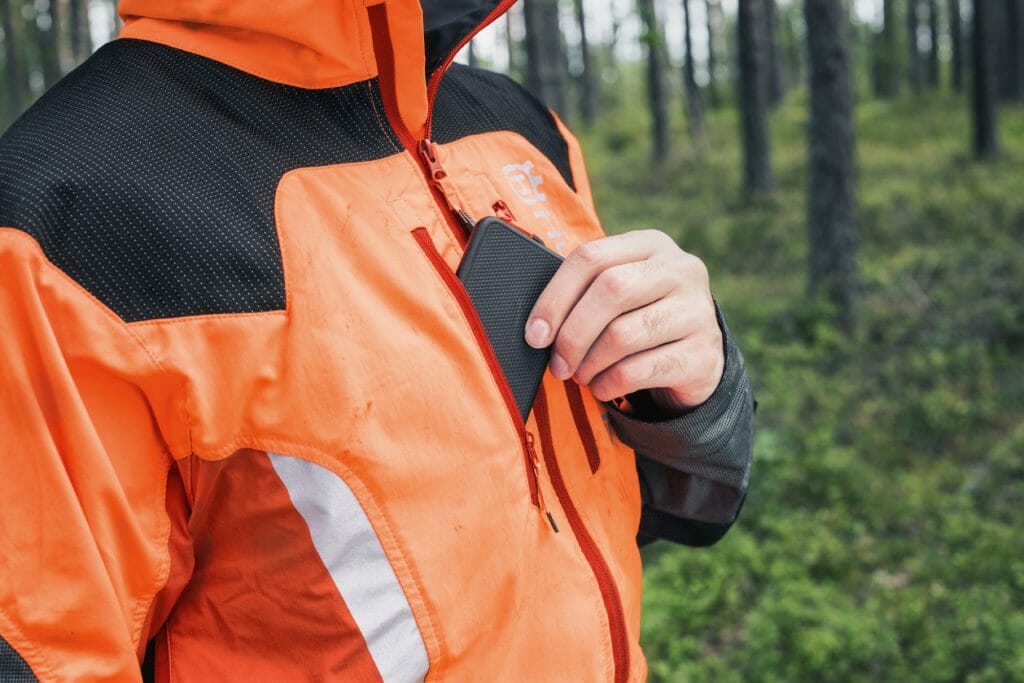 A mobile phone is taken out from a chest pocket of a forestry jacket