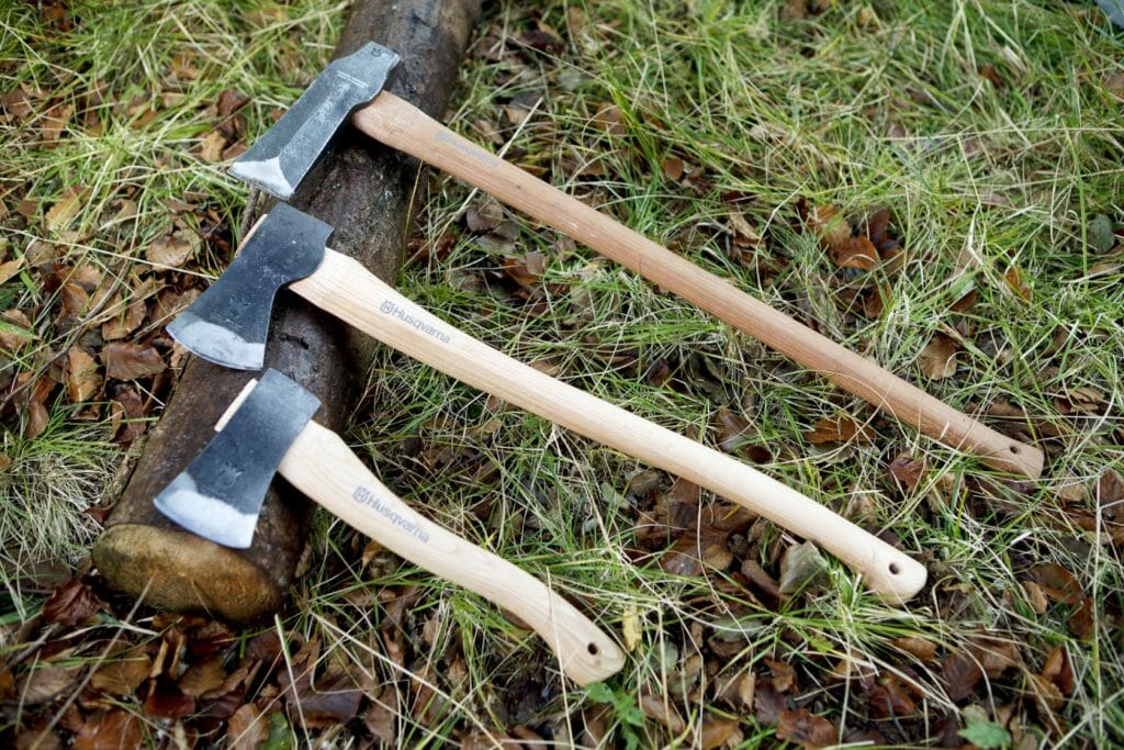 Tree axes in different sizes with wooden handles lying on a log on the ground