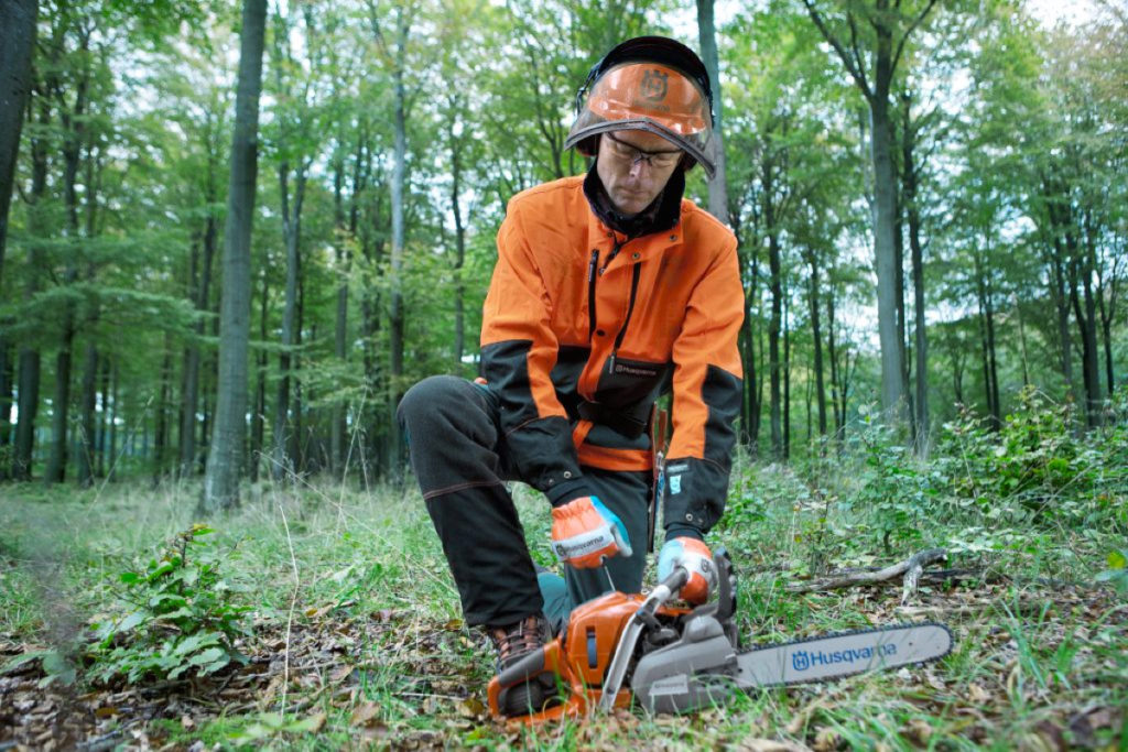 Forestry worker starting a chainsaw between his legs